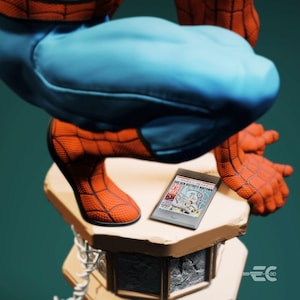May include: A detailed figurine of Spider-Man in a crouching pose, with red and blue costume. A small tablet displays a comic book cover with the headline "Doc Ock Destroys Midtown". The figurine rests on a stone-like pedestal.