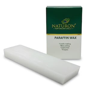 May include: Multi-Purpose Wax Slab. A white block of paraffin wax is positioned beside a green and white box. The box displays "NATURON" and "PARAFFIN WAX", with uses such as candle-making and crayon production. The wax block is rectangular.