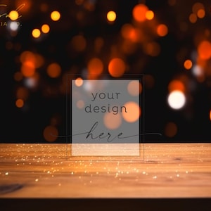 May include: A wooden table with a light brown surface and a scattering of gold glitter. The background is a dark blur with out-of-focus orange and white lights. The text "your design here" is in a white box.