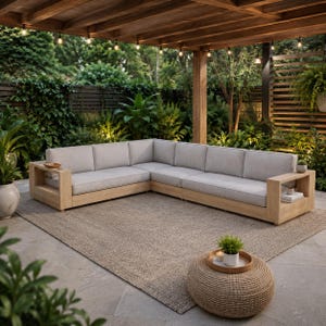 May include: A large L-shaped sectional sofa with a light wood frame and light gray cushions. The sofa features integrated side tables on both ends. A round, woven ottoman with a small potted plant and a candle sits in front of the sofa.