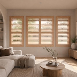 Könnte beinhalten: Drei hellfarbene Holzfensterläden mit horizontalen Lamellen, die an einer schlichten Wand montiert sind. Die Fensterläden sind als zwei schmale Seitenpaneele und ein breiteres Mittelpaneel angeordnet, wodurch natürliches Licht durch die Schlitze fällt.