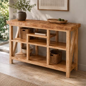 May include: A light brown wooden console table with a butcher block style top, featuring an open shelving design with X-shaped side supports. The unit includes two woven baskets, a ceramic bowl, and a book placed on the various interior shelves.