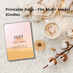 Könnte beinhalten: Eine Kindle-Hülle mit dem Text "JUST one more CHAPTER" in einem Wüstenlandschaftsdesign. Die Hülle befindet sich in einem transparenten Gehäuse. Das Bild enthält auch eine Tasse Kaffee, Trockenblumen und eine Decke.