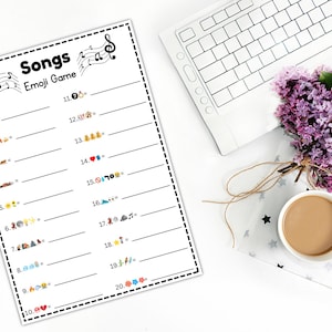 Peut inclure: Une feuille blanche imprim&eacute;e avec le jeu "Songs Emoji Game", des notes de musique et des lignes num&eacute;rot&eacute;es pour les r&eacute;ponses. Un clavier blanc, une tasse de caf&eacute; et un bouquet de fleurs violettes sont &eacute;galement dans l'image.