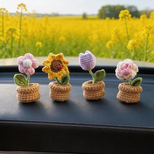 May include: Four small crocheted flowers in individual tan pots. The set includes a pink flower with a white center, a yellow sunflower with a brown center and a small red ladybug, a light purple tulip, and a pale pink rose, each with green leaves.