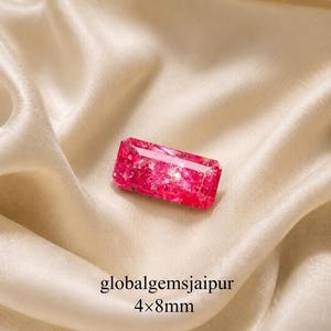 May include: A rectangular, vibrant pink gemstone with a textured surface, resting on a cream-coloured satin fabric. The gemstone measures 4x8mm. The text "globalgemsjaipur" and the dimensions are visible.