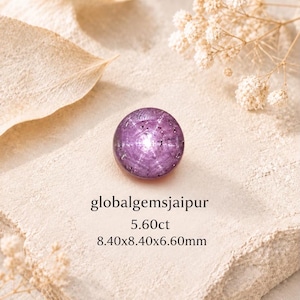 May include: A round, purple gemstone with a star-like pattern, labelled with the text globalgemsjaipur, 5.60ct, and 8.40x8.40x6.60mm. The stone features a cabochon cut with a bright, centred light reflection and internal inclusions.