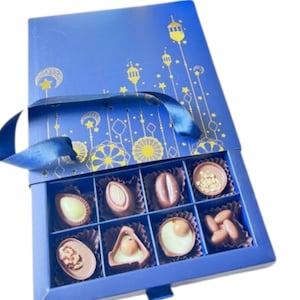 May include: A blue gift box with a ribbon, filled with assorted chocolates. The box lid features gold-colored decorative patterns. Each chocolate is in a small paper cup, showcasing various shapes and toppings.