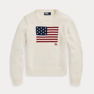May include: Cream-colored sweater featuring a red, white, and blue American flag design on the front. The flag has a field of white stars and red and white stripes. The letters "RL" are below the flag.