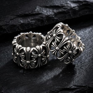 May include: Two silver rings with a repeating fleur-de-lis pattern. The rings are on a dark, textured surface. The rings have a .925 stamp.