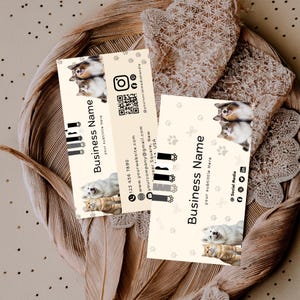 May include: Two rectangular business cards with a cream background featuring photos of a dog and cat, paw print patterns, and black text. The cards display Business Name, your subtitle here, contact details, social media icons, and a QR code.