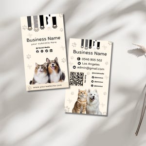 May include: Two rectangular business cards with a cream background featuring paw print patterns and animal paw graphics at the top. Each card displays Business Name, contact details, social media icons, a QR code, and photos of a cat and dog.