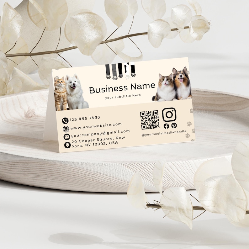 May include: A rectangular business card with a cream background featuring images of two cats and two dogs. The text reads Business Name, your subtitle Here, contact details, a QR code, and social media icons with the handle @yoursocialmediahandle.