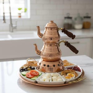 Könnte beinhalten: Eine kupferne Teekanne mit passendem Serviertablett. Die zweistöckige Kanne hat Holzgriffe und steht auf einem Tablett mit kleinen weißen Schalen mit Lebensmitteln, darunter Oliven, Tomaten und Käse. Das Tablett ist kupferfarben.