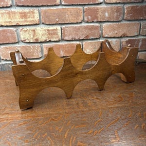 May include: A wooden wine rack with a warm, medium-brown finish. The rack is designed to hold multiple bottles, featuring a series of curved supports. The design is simple and functional, suitable for home decor. The rack is placed on a wooden surface.
