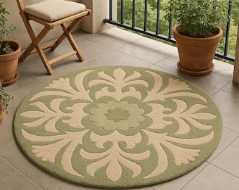 May include: A round outdoor rug with a floral design in shades of green and beige. The rug is placed on a tiled patio, with a wooden folding chair and potted plants in the background. The rug's diameter is approximately 60 inches.