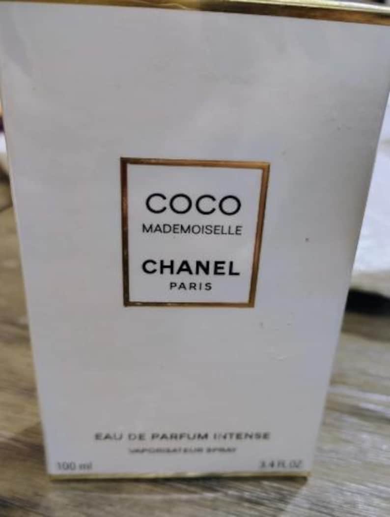 May include: White rectangular box with gold trim featuring the text "COCO MADEMOISELLE CHANEL PARIS". The box also indicates "EAU DE PARFUM INTENSE" and "3.4 FL. OZ". The box is for a fragrance product.