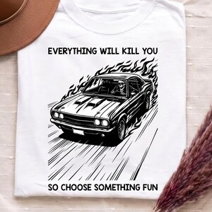 Może przedstawiać: Biała koszulka z czarną grafiką klasycznego samochodu w płomieniach. Tekst "EVERYTHING WILL KILL YOU SO CHOOSE SOMETHING FUN" jest wydrukowany. Brązowy kapelusz i suszone kwiaty również znajdują się na zdjęciu.