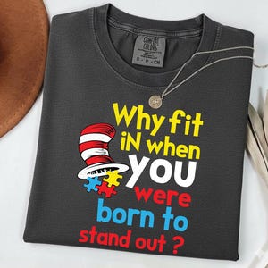 May include: Dark gray t-shirt with the text "Why fit IN when YOU were born to stand out?" and a Dr. Seuss-style hat graphic. The shirt has a crew neck and a small tag at the neckline.