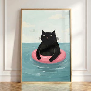 May include: A framed art print featuring a black cat floating in a pink inflatable ring in a body of water. The cat has yellow eyes and is set against a light blue sky with white clouds. The water is a light blue color.