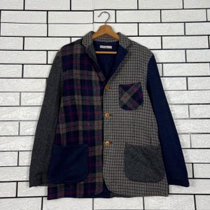 Könnte beinhalten: Ein Patchwork-Blazer mit einzigartigem Design. Die Jacke hat eine Mischung aus grauen, marineblauen und karierten Mustern. Sie hat zwei Vordertaschen und Holzknöpfe. Die Ärmel sind einfarbig grau und der Kragen ist marineblau.