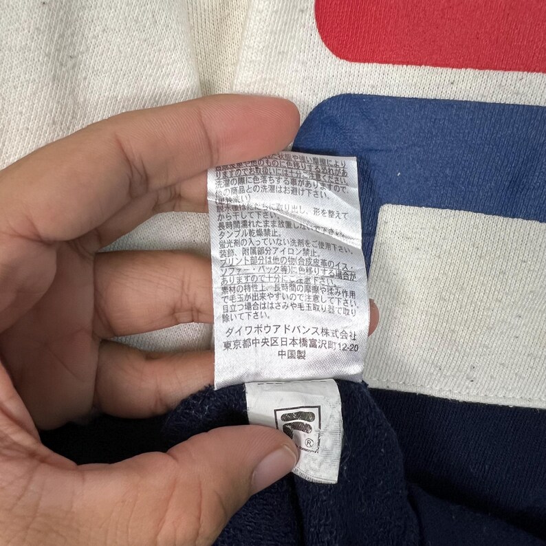 May include: Close-up of a navy blue and red garment with a white tag. The tag has Japanese text and a logo. The garment has a white tag with Japanese text and a logo.