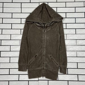 May include: A brown hooded zip-up jacket with two front pockets. The jacket has a full-length zipper and a drawstring hood. The fabric has a textured appearance. The jacket is displayed against a white brick wall.