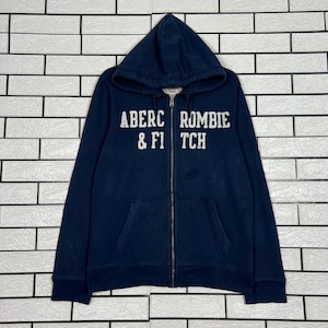 May include: A navy blue hooded zip-up sweatshirt with a front pocket. The white text "Abercrombie & Fitch" is printed across the chest. The sweatshirt is made of a soft material.