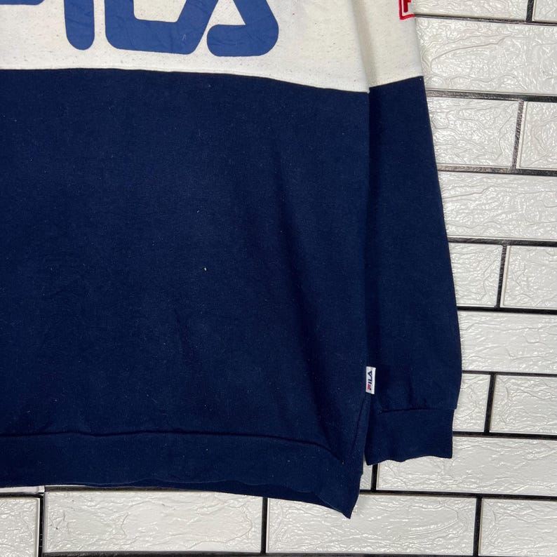 May include: A navy blue and white sweatshirt with the brand name in large blue letters across the chest. The sweatshirt has a color block design, with the top portion white and the bottom navy blue. The brand logo is visible on the sleeve.