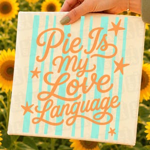 May include: A square canvas sign featuring vertical light blue stripes on a cream background. The text "Pie Is my Love Language" is written in a large, orange, cursive script. Four orange starfish icons are positioned around the text.