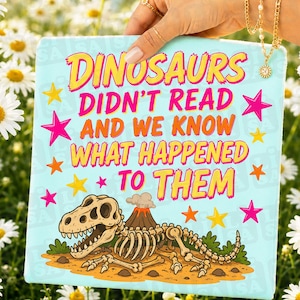 May include: A light blue square with the text "DINOSAURS DIDN'T READ AND WE KNOW WHAT HAPPENED TO THEM" in yellow and orange. The image includes a cartoon dinosaur skeleton and a volcano. Pink and yellow stars decorate the background.
