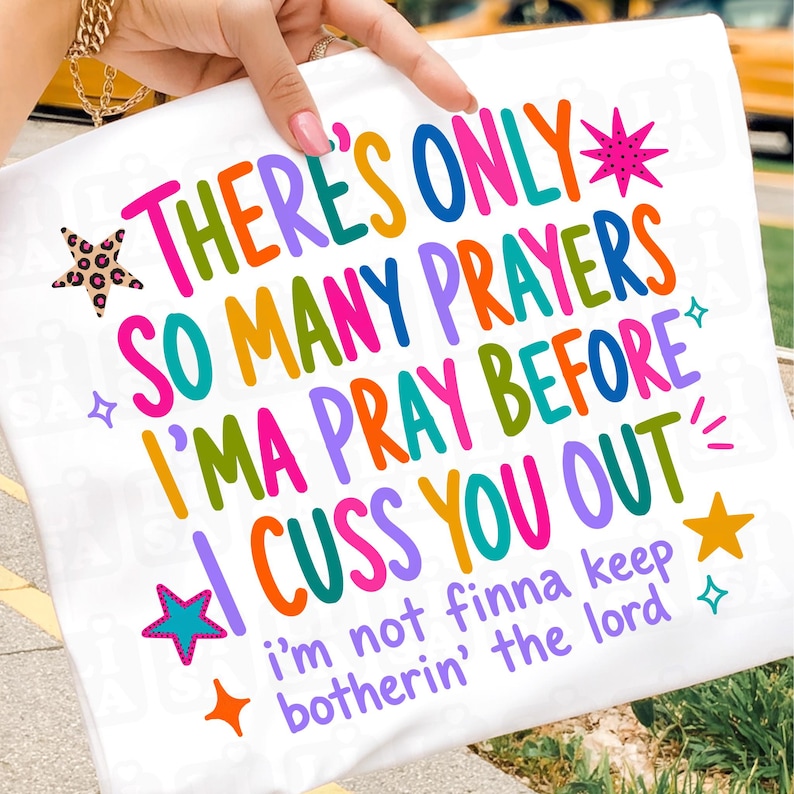 May include: A white t-shirt featuring colorful text that reads: THERE'S ONLY SO MANY PRAYERS I'MA PRAY BEFORE I CUSS YOU OUT and i'm not finna keep botherin' the lord. The design includes various multi-colored stars and small sparkle icons.