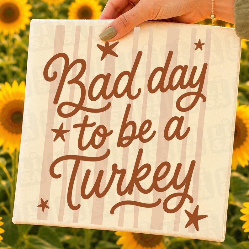 May include: A square canvas sign featuring a cream background with vertical light beige stripes. The text "Bad day to be a Turkey" is printed in a dark brown cursive font, accented by four small dark brown stars positioned around the text.