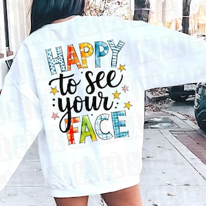 Może przedstawiać: Biała bluza z napisem "HAPPY to see your FACE" w kolorowych, zabawnych literach. Projekt zawiera gwiazdki i różne wzory w literach, tworząc wesoły wygląd. Swobodny, wygodny element garderoby.