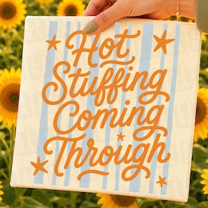 May include: A square canvas sign featuring vertical light blue stripes on a cream background. The text "Hot Stuffing Coming Through" is written in a bold, orange, cursive script, accented by four small orange stars positioned at the corners.