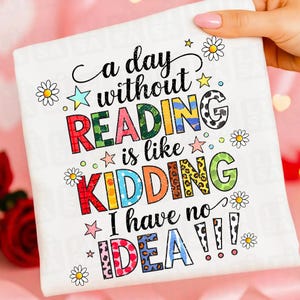 Może przedstawiać: Biała poduszka z kolorowym napisem "a day without READING is like KIDDING I have no IDEA!!!". Ozdobiona stokrotkami i gwiazdkami.