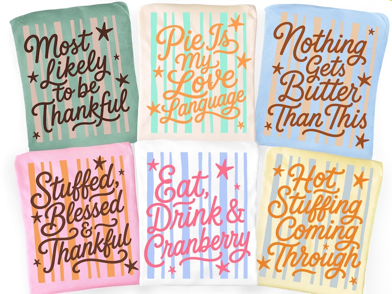 May include: Six folded t-shirts in various pastel colors, each featuring vertical stripes and star accents. The shirts display phrases including Most Likely to be Thankful, Pie Is my Love Language, Nothing Gets Butter Than This, Stuffed Blessed & Thankful, Eat, Drink & Cranberry, and Hot Stuffing Coming Through.