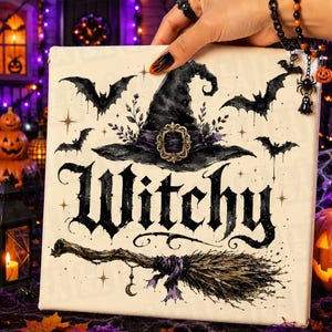 May include: A square canvas print featuring a black witch hat with a gold buckle, surrounded by flying bats and floral accents. The word Witchy is printed in large black gothic lettering above a broomstick with a small crescent moon charm.