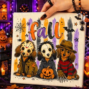 May include: A square canvas print featuring the word fall in orange and purple letters above three dachshunds dressed as horror movie characters. The dogs wear a hockey mask, a cracked white mask, and a brown fedora with a striped sweater.
