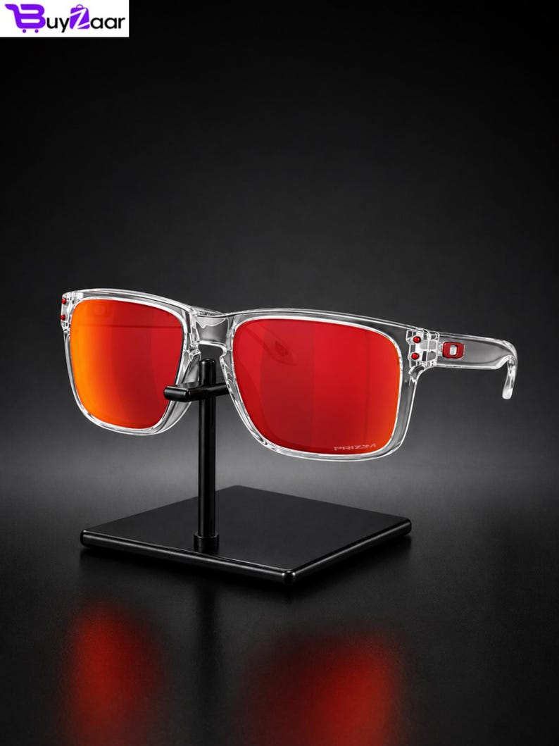 K&ouml;nnte beinhalten: Eine Sonnenbrille mit transparentem Rahmen und leuchtend roten Gl&auml;sern wird auf einem schwarzen St&auml;nder pr&auml;sentiert. Die rechteckigen Gl&auml;ser haben eine leichte Kr&uuml;mmung, und der Rahmen ist transparent. Der Hintergrund ist dunkel.