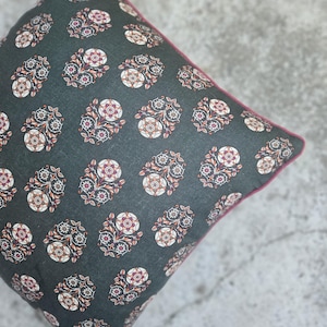 Könnte beinhalten: Ein quadratisches Kissen mit dunkelgrünem Hintergrund und einem sich wiederholenden Blumenmuster in Weiß, Rot und Braun. Das Kissen hat eine rosa Umrandung.