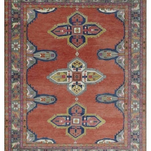 May include: A rectangular, hand-woven rug with a terracotta-colored field and a detailed border. The rug features a central design of stylized floral and geometric motifs in shades of blue, yellow, and gray. The border includes floral and geometric patterns.