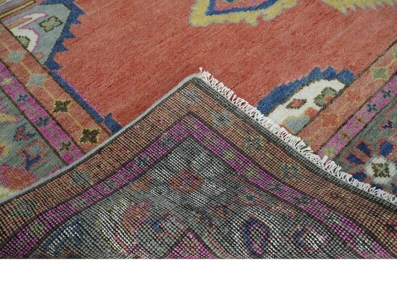 May include: A section of a vintage rug with a warm, reddish-orange central field. The rug features intricate geometric patterns in shades of blue, pink, and green, with a detailed border. The rug's edges are frayed, showing its age and use.