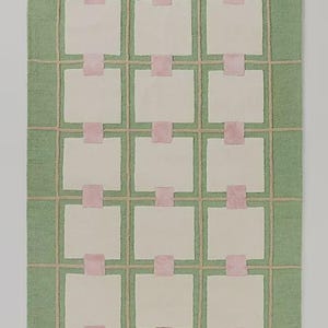 May include: A rectangular rug with a light green background and a grid pattern in a tan color. The rug features off-white squares connected by pink rectangles, creating a geometric design. The rug is a decorative home accent.