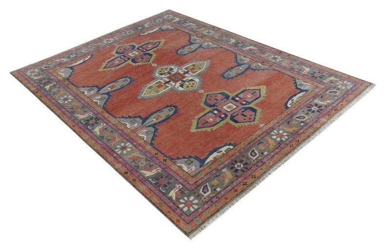 May include: A square, red rug with a detailed border and central design. The rug features a repeating pattern of stylized floral and geometric shapes in shades of blue, green, and cream. The border is a mix of floral and geometric elements.