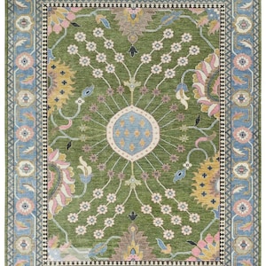 May include: A rectangular rug with a detailed floral pattern. The central field is green, adorned with flowers and leaves in pink, blue, yellow, and brown. The border is light blue with floral motifs. The rug's design is intricate and ornate.