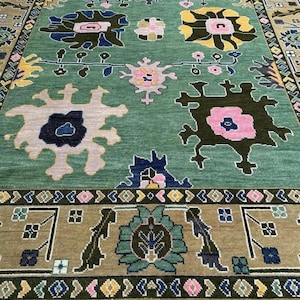 May include: A green rug with a floral design. The rug displays large, stylised flowers in pink, yellow, and blue against a green backdrop. The border is a darker shade of green and brown with geometric and floral patterns. The rug has a fringe.