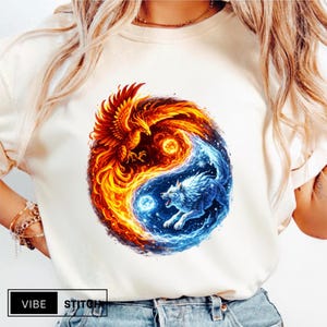 Könnte beinhalten: Cremefarbenes T-Shirt mit Yin-und-Yang-Design. Eine Seite zeigt einen feurigen orange-roten Phönix, die andere einen blauen Wolf. Auf dem Shirt steht unten der Text "VIBE STITCH".
