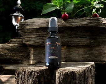 May include: A black bottle of beard oil with a spray nozzle. The label reads "Wit's End" with a purple octopus design. The bottle is set on a wooden surface with a natural background.