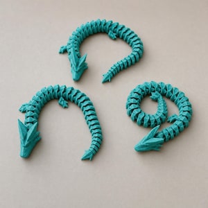 May include: Three teal-colored articulated dragon figurines with segmented bodies and detailed heads. Each dragon features a flexible, multi-part design with visible joints, allowing for movement. The figures are arranged in different curved positions.
